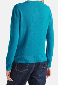 Turkos stickad tröja med ribbade mudd och nederkant, med rund halsringning och mjuk textur. Bärs med mörka jeans.