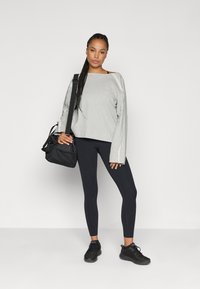 Γκρι κοντό φούτερ με μακριά μανίκια, συνδυασμένο με μαύρες κολάν και μαύρα αθλητικά παπούτσια. Το μοντέλο κρατά μια μαύρη τσάντα με λουρί.