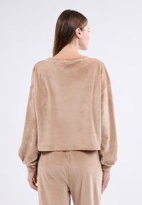 Beżowy sweter w stylu cropped z korduroy, z długimi, bufiastymi rękawami i prążkowaną strukturą. Z tyłu znajduje się szeroki dekolt i subtelny połysk.