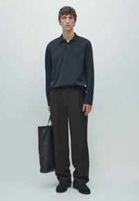 Granatowa koszulka polo z długim rękawem i kołnierzykiem, zestawiona z luźnymi czarnymi spodniami i czarną skórzaną torbą typu tote. Modelka nosi czarne buty.