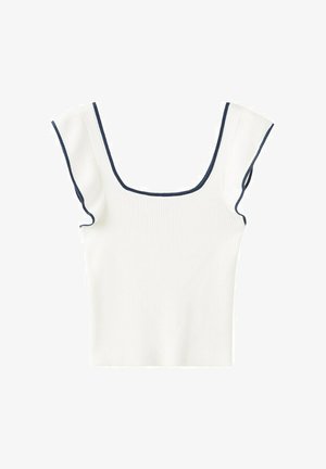 Młoda kobieta nosząca biały bezrękawnik z kwadratowym dekoltem, niebieskie dżinsowe szorty z wiązaniem po boku i czarne sandały na paski, stojąca na jednolitym tle.