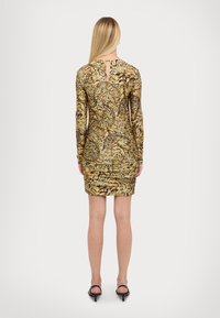 Långärmad klänning i ett gult och svart djurmönster, med en figurnära passform, nyckelhålsdetalj på baksidan och rynkat nederkant.