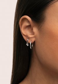 Pendientes de aro plateados con un pequeño charm en forma de estrella, que presentan un acabado pulido y una textura suave, luciendo en la oreja de una persona.