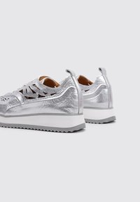 Zapatillas metálicas plateadas con un acabado texturizado, suela de goma gris claro y diseño troquelado en los laterales para ventilación.