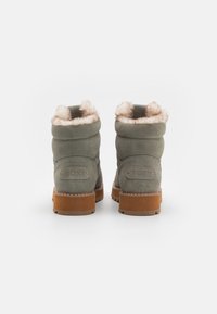 Bottines en daim vert avec une doublure en fausse fourrure, semelle en caoutchouc beige, et détail de logo embossé sur le talon. Finition texturée et douce.