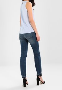 Haut sans manches bleu clair associé à un jean skinny bleu foncé. Le haut présente un col rond et une subtile découpe au dos. Chaussures à talons hauts noires.