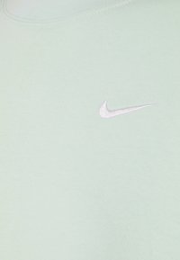 Tissu vert clair avec un petit logo Nike swoosh blanc brodé sur la partie supérieure de la poitrine.