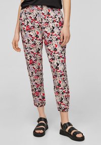 Pantalon à imprimé floral avec une base rose clair, comportant des fleurs rouges, noires et violettes ; taille élastique ; jambe fuselée ; porté avec des sandales noires.