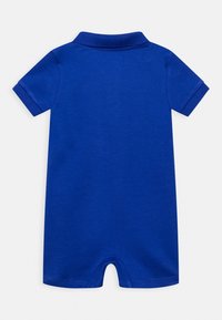 Modrý bavlněný overal s polo límcem, krátkými rukávy a hladkou texturou. Uzavřený ve spodní části s otevřeným designem nohou.