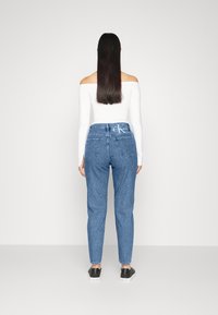 Blå högmidjade jeans med tapered ben, med bakfickor, knappstängning och bälteshällor, i kombination med en vit långärmad topp.