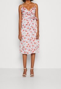 Robe midi fleurie présentant un fond rose avec des fleurs rouges et bleues, un design portefeuille, des bretelles spaghetti réglables et un détail de nouage sur le côté.