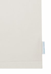 Nærbilde av et kremfarget stoff med en hvit etikett på høyre kant som har teksten "COUCH COUTURE" i blått.