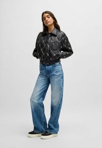 Black quilted puffer jacket with a snap-front closure, large collar, and one chest pocket. Paired with wide-leg faded blue jeans and black sneakers.