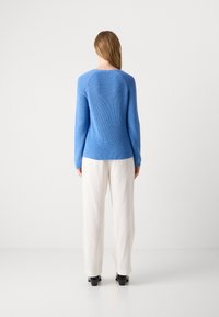 Maglione blu a maglia con maniche lunghe, texture a coste e scollatura rotonda. Abbinato a pantaloni bianchi a gamba larga e tacchi neri.