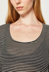 Černobílé pruhované tričko s kulatým výstřihem a průsvitnou texturou, které má střídavé vodorovné pruhy různé tloušťky.