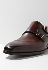 Chaussure monk en cuir marron avec un bout pointu élégant, deux boucles métalliques et une finition lisse. Coutures remarquables aux bords.