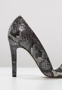 Svart och gråt mönstrad högklackad sko med spetsig tå och smal stilettklack. Texturerad läderyta.