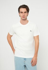 Biele bavlnené tričko s okrúhlym výstrihom, krátkymi rukávmi a malým čiernym logom na ľavej strane hrudníka. Kombinované s svetlomodrým denimom.