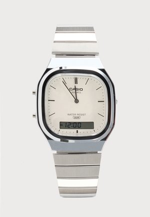 Montre-bracelet Casio argentée avec affichages analogique et numérique, affichant 12h00, étiquetée quartz et résistante à l'eau avec un bracelet en métal à maillons.