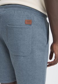 Shorts en coton bleu clair avec une finition texturée, dotés d'une poche arrière et d'un patch en cuir marron portant l'inscription "BLEND". Ceinture douce.