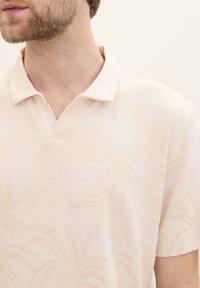 Kortärmad pikétröja i ljusbeige med ett texturerat palmbladsmönster, med en klassisk krage och en mjuk tygfinish.