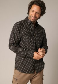 Zwarte langemouwenshirt met een gouden geometrisch patroon, knoopkraag, twee borstzakken en een relaxte pasvorm. Getextureerde stof.