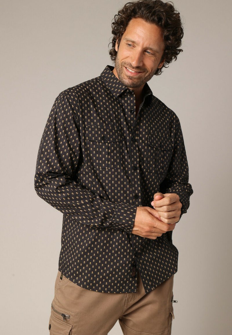 Zwarte langemouwenshirt met een gouden geometrisch patroon, knoopkraag, twee borstzakken en een relaxte pasvorm. Getextureerde stof.