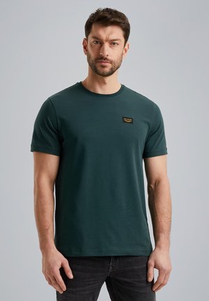 Green crew-neck t-shirt made of cotton, featuring short sleeves and a small black branding label on the chest. Smooth texture, fitted shape.