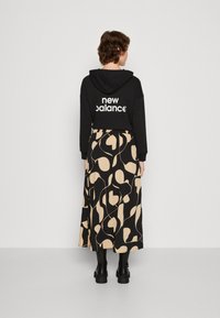 Corta hoodie preta com o logótipo "new balance", emparelhada com uma saia midi com um padrão abstracto bege sobre um fundo preto. Botas pretas grossas.