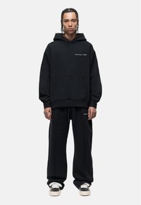 Zwart hoodie en trainingsbroek set, gemaakt van zachte stof. Bevat een voorkant pocket, een taille met trekkoord en contrasterende stiksels.
