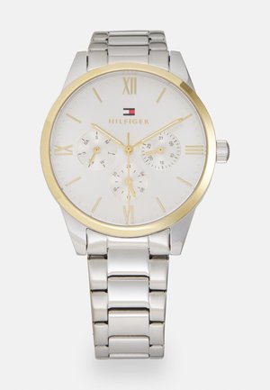 Montre en acier inoxydable argenté avec un cadran blanc, accents dorés, marqueurs en chiffres romains et trois sous-cadrans ; bracelet en maillons métalliques.