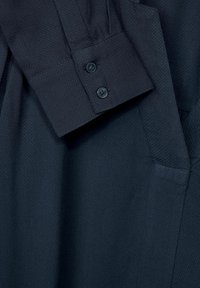 Manche de chemise bleu marine foncé avec deux boutons noirs et détail de tissu texturé visible en gros plan.