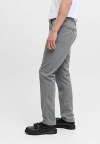 Pantalones grises de mezcla de algodón, diseño de pierna recta, parte delantera plana, detalles en el bolsillo trasero, combinados con zapatos negros brillantes.