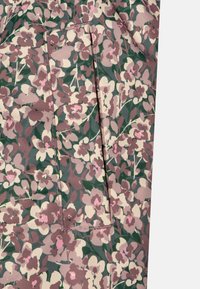 Blommönstrad tyg med rosa och krämfärgade blommor på en grön bakgrund och en fickdetalj. Mjuk textur och lätt material.