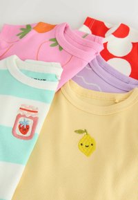 Chemises en maille côtelée pliées de couleurs pastel avec des motifs brodés ludiques de fruits et de fleurs sur la zone de l'encolure avant.