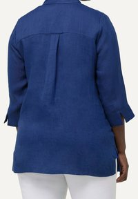 Blå linneskjorta med trekvartslånga ärmar, bakklaff och sidslitsar för rörelsefrihet. Slät textur och avslappnad passform.