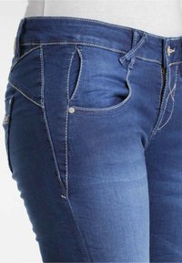 Mörkblå denimjeans med en slät yta, med en figursydd design, detaljerad sömnad och fem fickor, inklusive en myntficka.