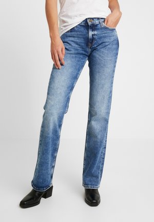 Blaue Jeans aus Denim mit geradem Schnitt, mittelhoher Taille, heller Waschung und subtilen Ausbleichungen. Schwarze Absatzschuhe runden den Look ab.