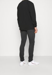 Camisa negra de manga larga, jeans ajustados grises, zapatillas blancas con detalles rojos. Diseño sencillo, textura suave, ajuste relajado.