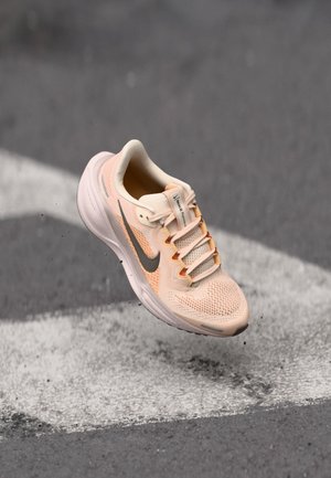 Pantof cu un design de piersici deschis, cu un capac din plasă, logo gri Swoosh, șireturi plate și o talpă amortizată, poziționat deasupra unei linii pictate pe stradă.