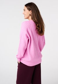 Losse, geribbelde roze trui met ballonmouwen en een brede halslijn, gecombineerd met donkere broek. Zachte knit textuur, ontspannen silhouet.