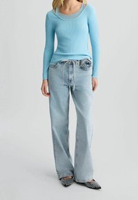 Haut à manches longues bleu clair côtelé avec un col rond, associé à un jean large délavé clair et des chaussures noires pointues ornées de détails.