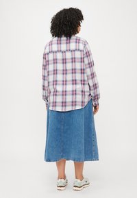 Cămașă din flanel în carouri în nuanțe de alb, albastru și roz, asociată cu o fustă maxi din denim deschis și adidași albi cu accente verzi.