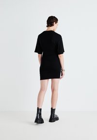 Melnas īso piedurkņu kleitas ar pieguļošu siluetu. Gluda auduma, virs ceļgala garuma, valkāta ar masīvām melnām potīšu zābakiem. Minimālistisks dizains.