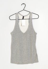 Šedý tílko s hlubokým véčkovým výstřihem a síťovaným vzorovaným zadním dílem. Navrženo s širokými ramínky a připevněnou visačkou. Jemná textura látky.