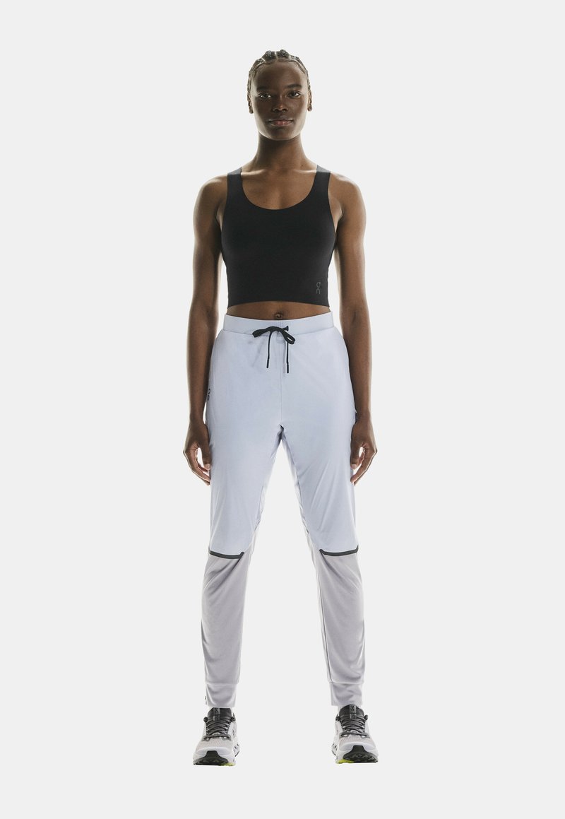 Sujetador deportivo negro con tirantes anchos, combinado con pantalones deportivos gris claro que cuentan con una cinturilla elástica y detalles en negro.