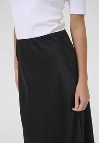 Jupe noire texturée en tissu lisse, dotée d'une taille haute, de poches latérales et d'une silhouette fluide.