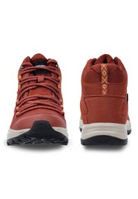 Punaiset vaelluskengät, joissa on tekstuuripinta, verkkoakselit ja keltaiset nauhat. Varustettu tukevalla kumipohjalla ja geometrisella muotoilulla takana.