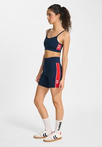 Haut court de sport bleu marine et shorts taille haute avec panneau latéral rouge et rayures blanches. Assorti à des chaussettes blanches et des baskets avec des accents bleus.