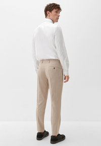 Tan broeken met een rechte snit, voorzien van een knoopzak aan de achterkant. Gekocht met een wit overhemd met lange mouwen en zwarte sneakers.